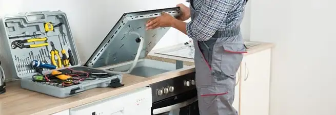 Cooktop repair technician lifting a built-in stovetop for service in Norfolk, VA