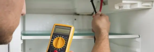Refrigerator repair technician testing electrical components with a multimeter in Norfolk, VA